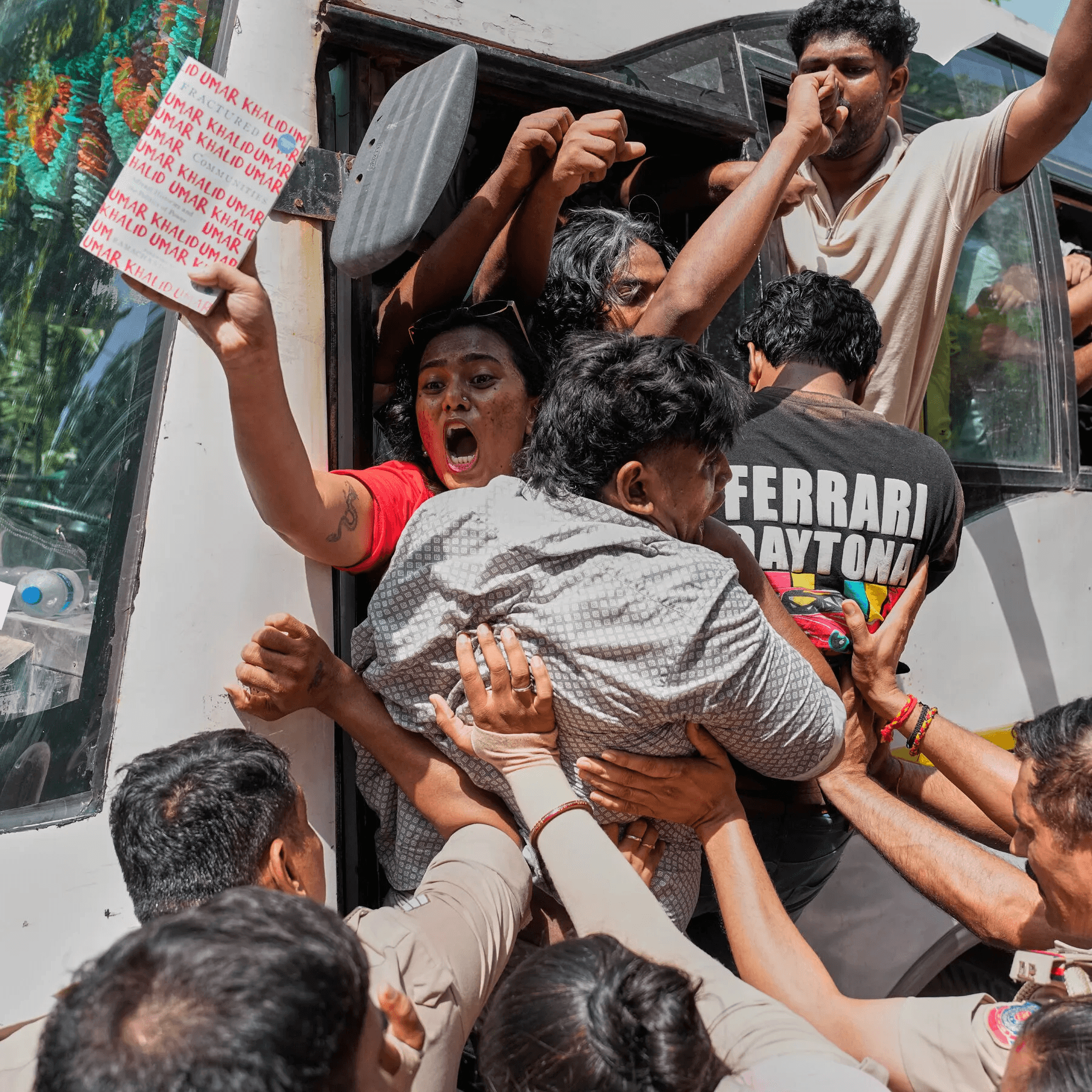 Protesters raising their fists and holding a sign near a vehicle.